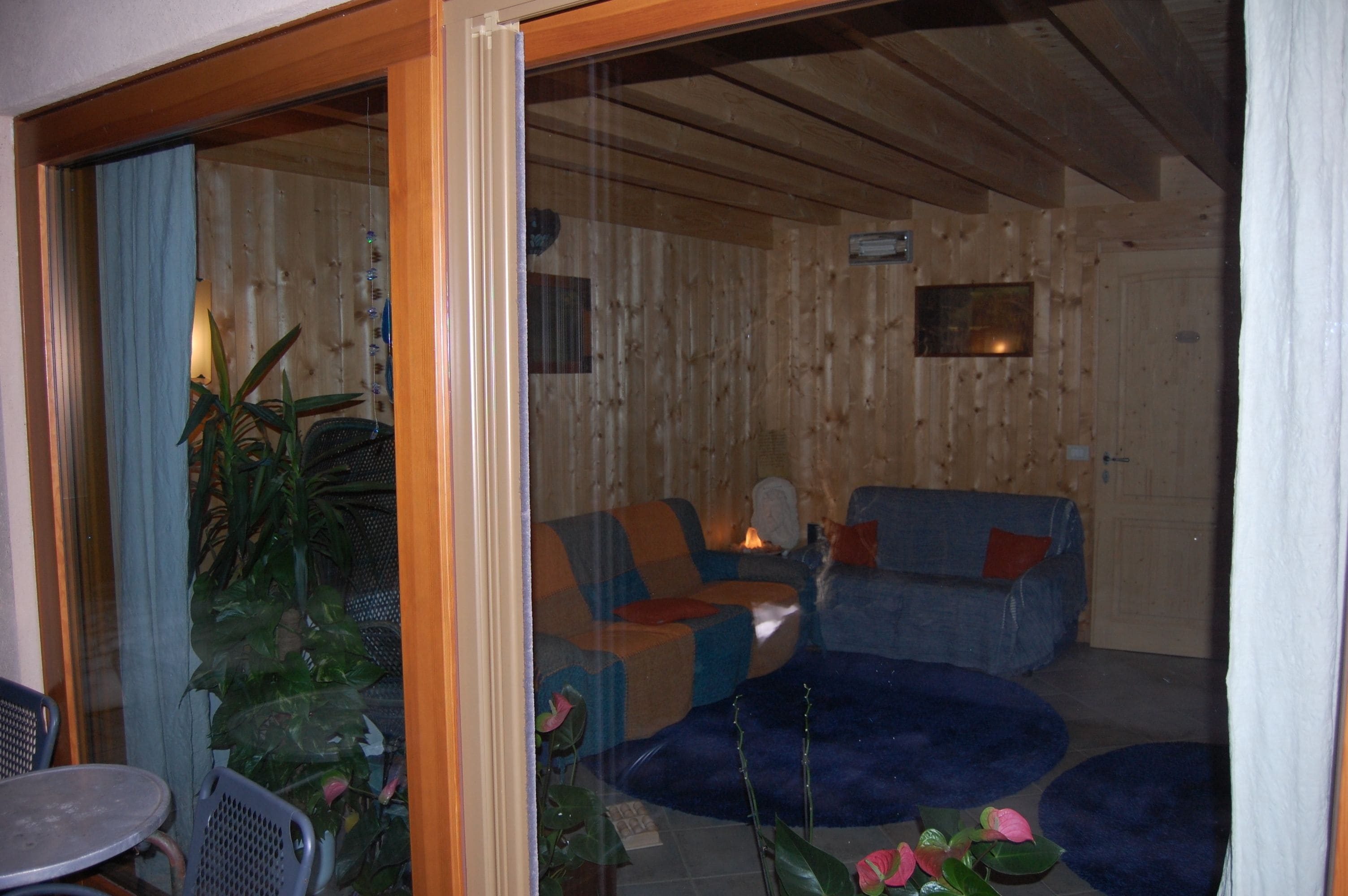 A cozy living area with a sofa, a coffee table, and a chair. There is a wooden wall and a glass door leading outside.