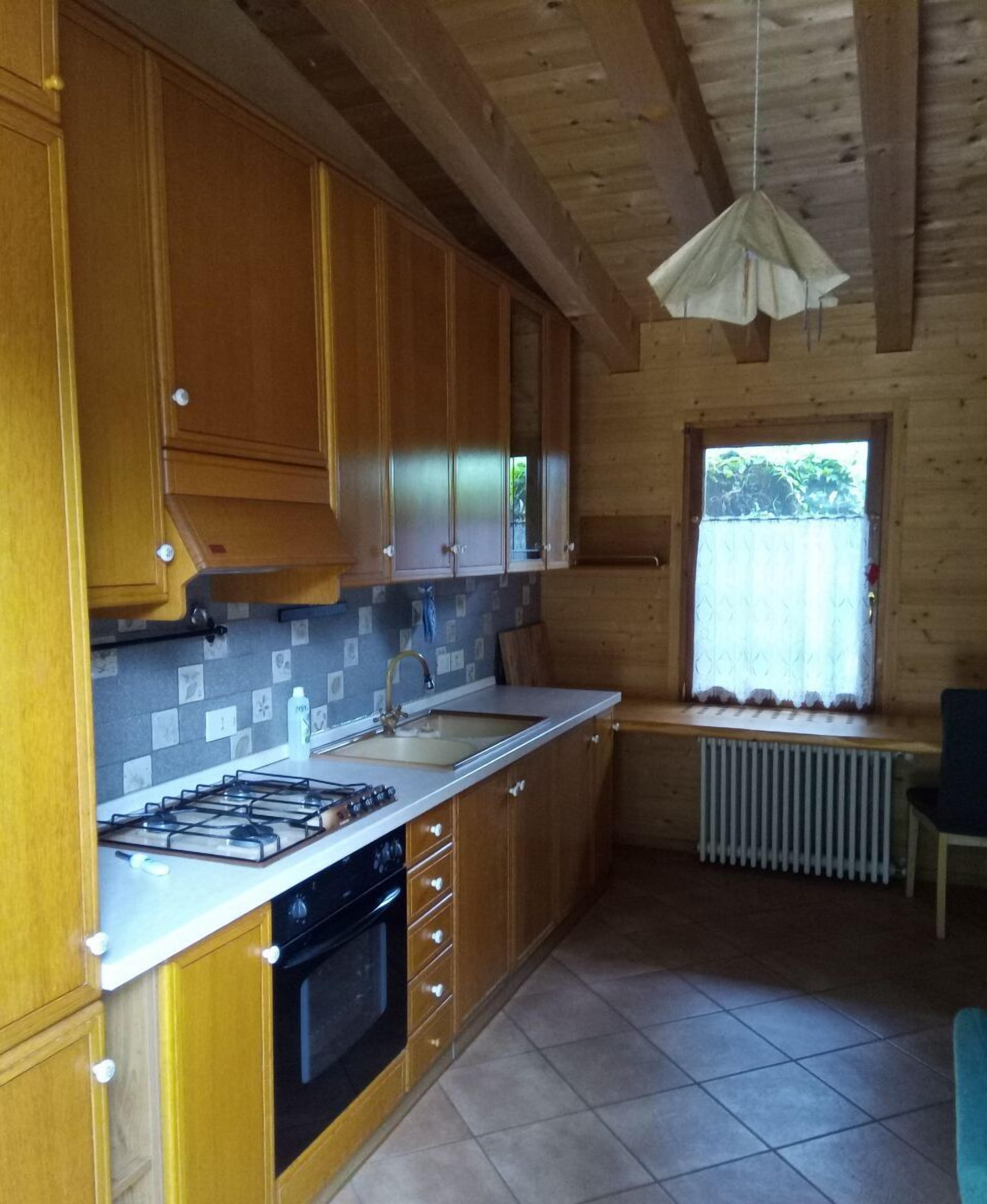 A kitchen with wooden cabinets, a gas stove, a sink, and a window with a curtain.