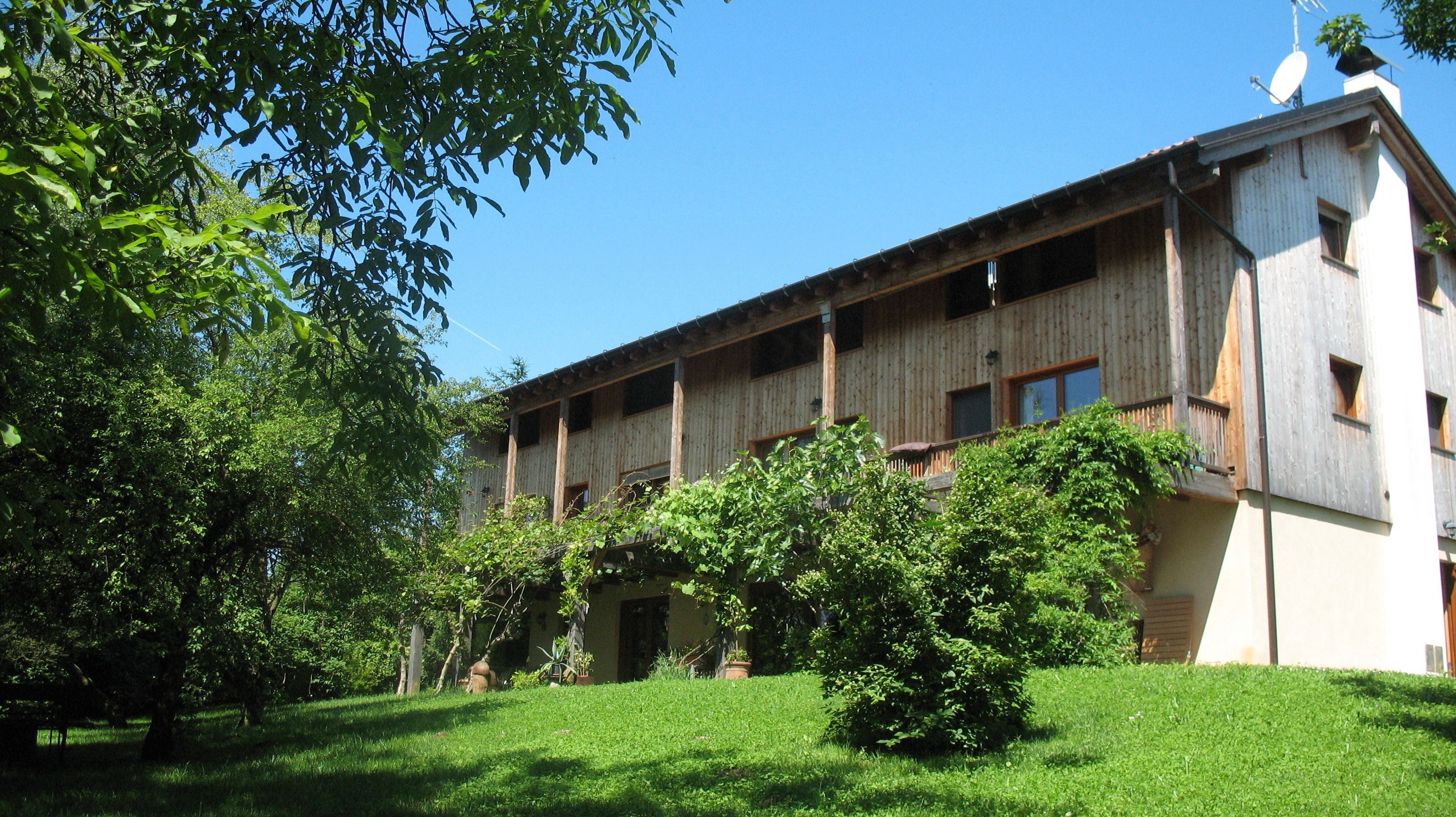 A rustic wooden building with multiple windows and a balcony, surrounded by lush greenery.