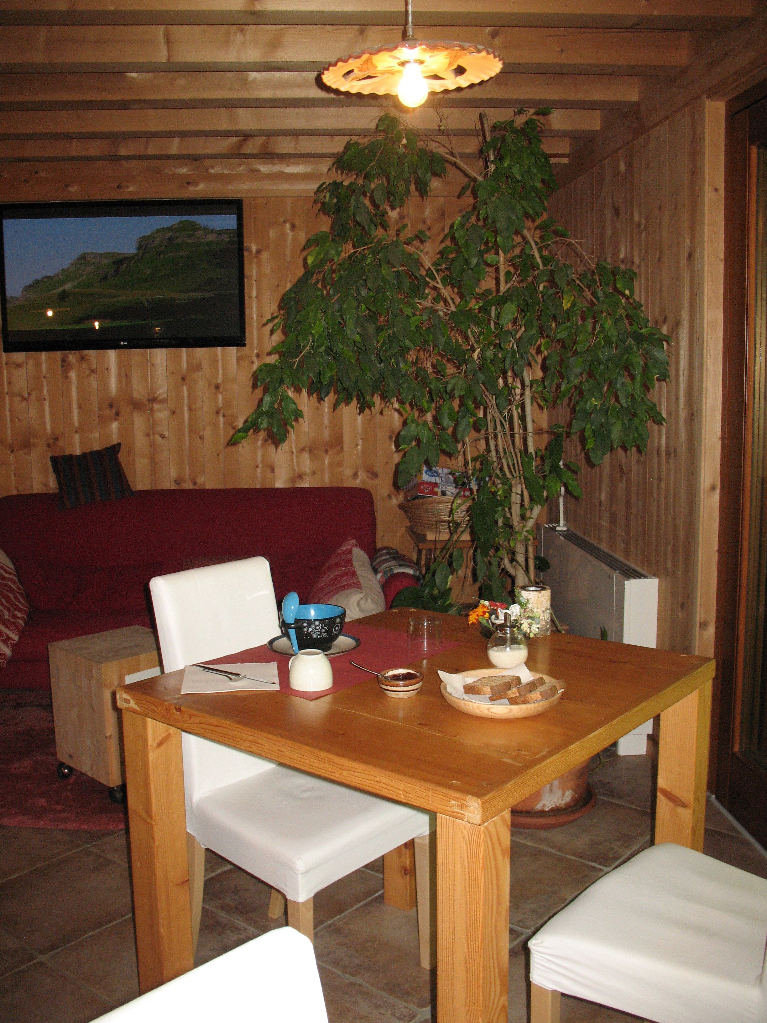 Ein Holzinnenraum mit einem Esstisch, Stühlen, einer Couch und einem an der Wand befestigten Fernseher.