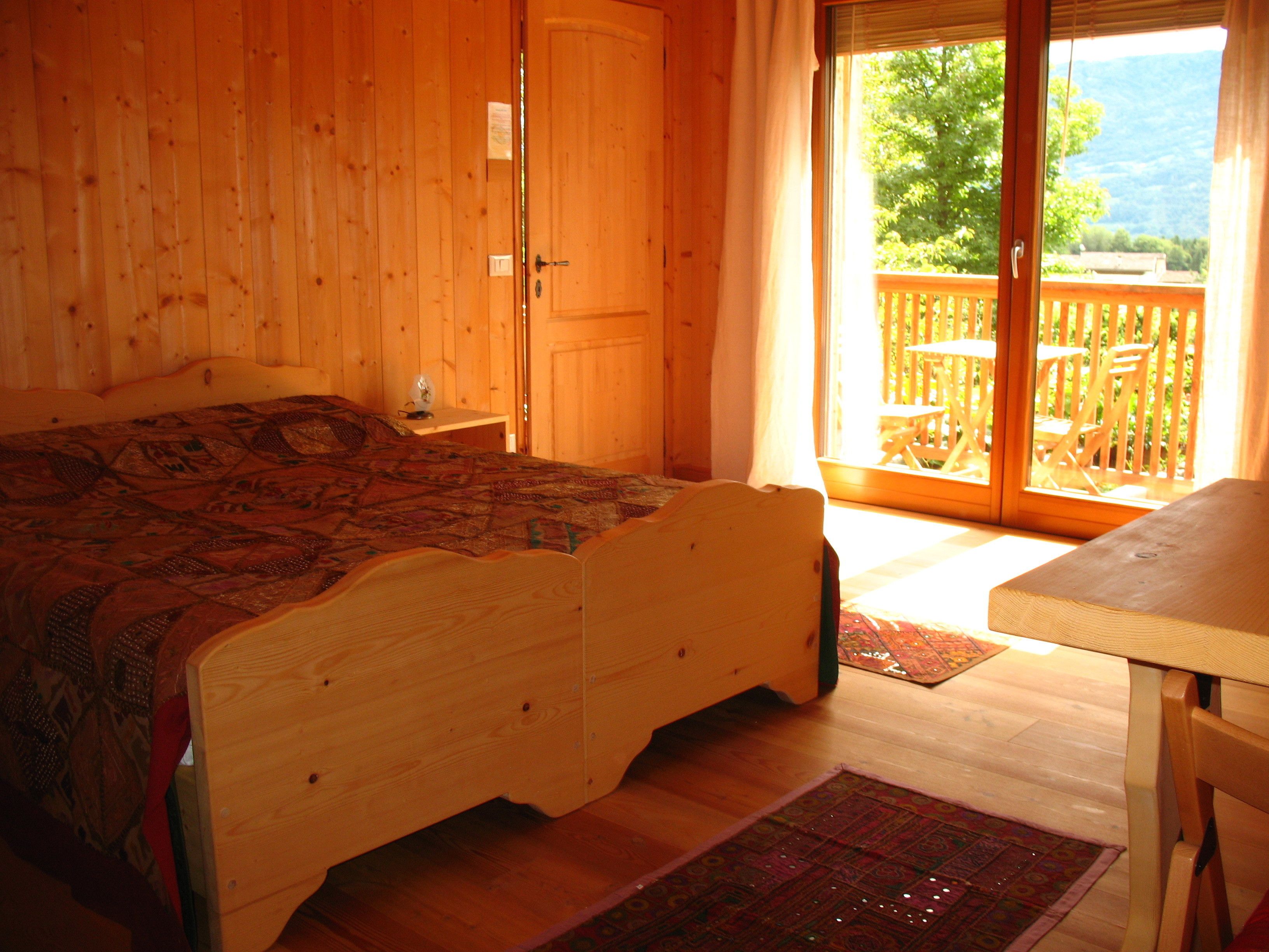 A wooden room with a bed, a small table, and a sliding glass door leading to an outdoor deck.