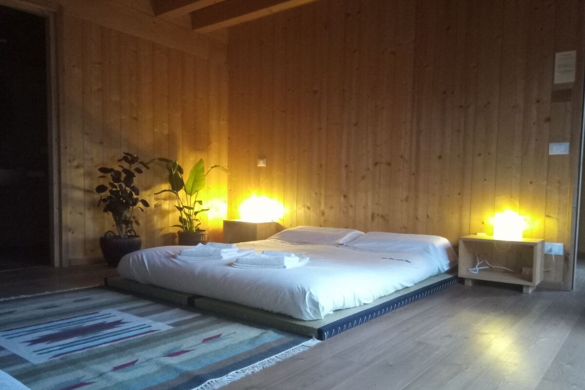 Een slaapkamer met een groot bed, houten wanden, twee nachtkastjes met lampen en een potplant.