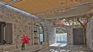 Un espacio al aire libre con paredes de piedra, con una mesa y sillas, un florero y vistas a una piscina.