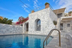 A pool area with a stone wall and a metal pool ladder. - Thermes Saint Alexander Villas (Santorini)