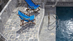 Un área de piscina de piedra con sillones reclinables azules y una escalera de piedra que conduce a un nivel superior.