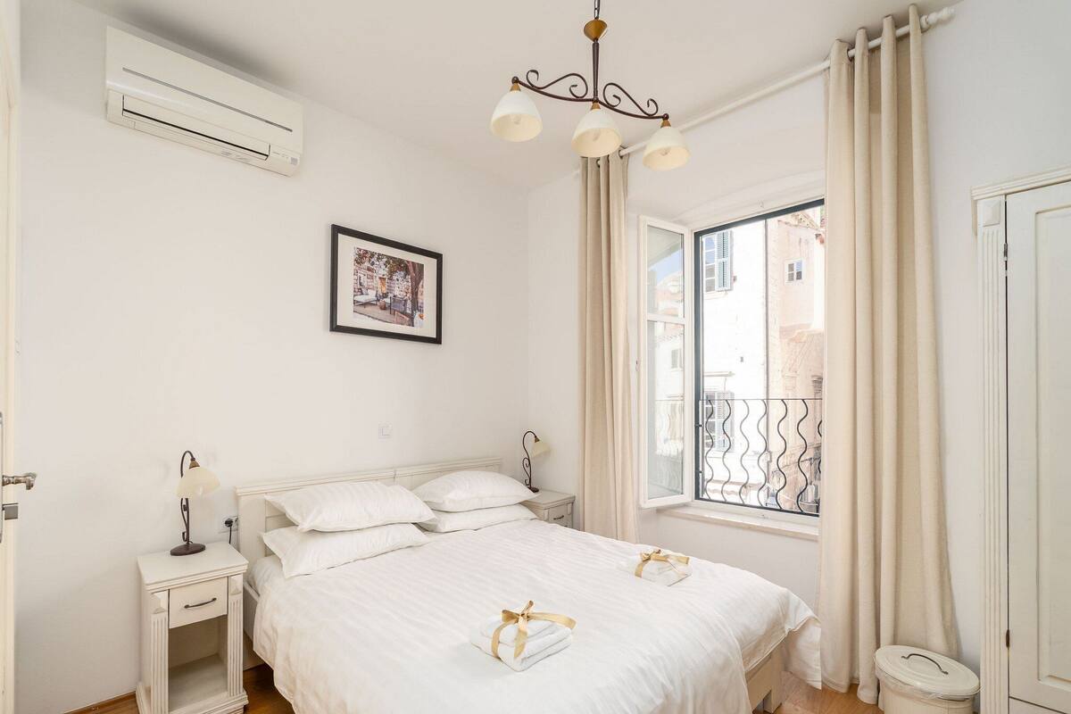 Una camera da letto con un letto, comodini, un quadro appeso, una finestra con tende e un termosifone.