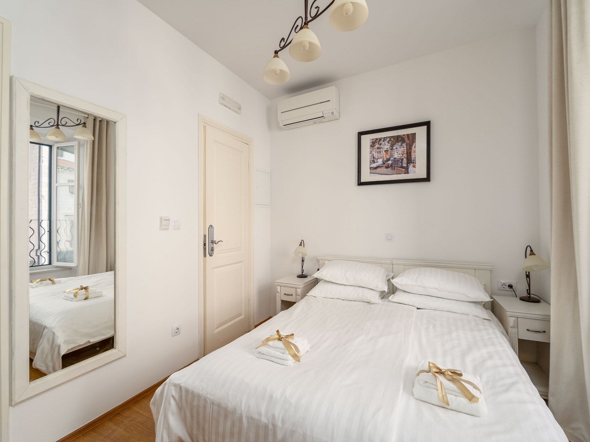 Habitación de hotel con una cama grande, mesitas de noche, un espejo, un equipo de aire acondicionado y un cuadro en la pared.