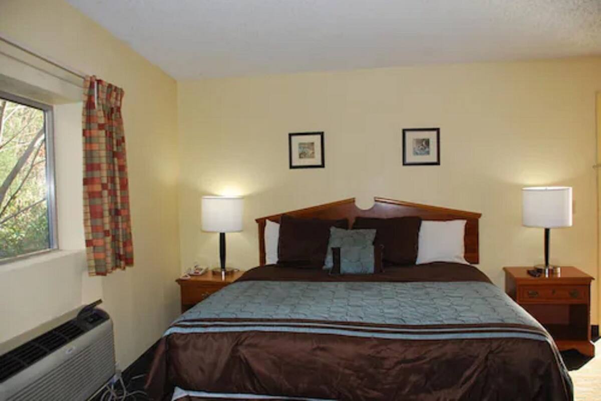 A bedroom with a large bed, two bedside tables, a window with curtains, and a radiator.