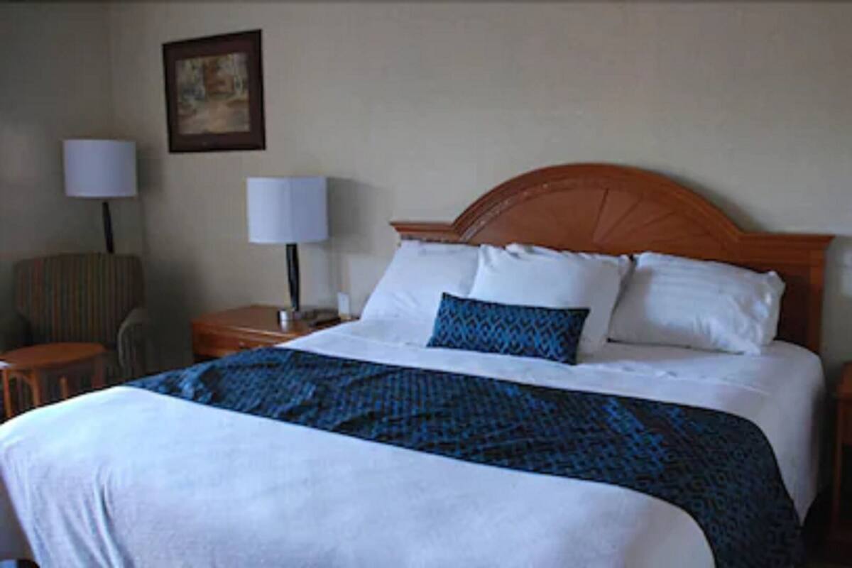 A neatly made bed with a wooden headboard, two bedside tables with lamps, and a chair.