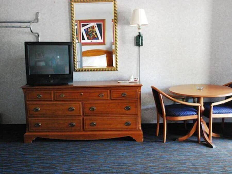 A hotel room with a wooden dresser, a television, a round table with two chairs, a lamp, and a framed picture on the wall.