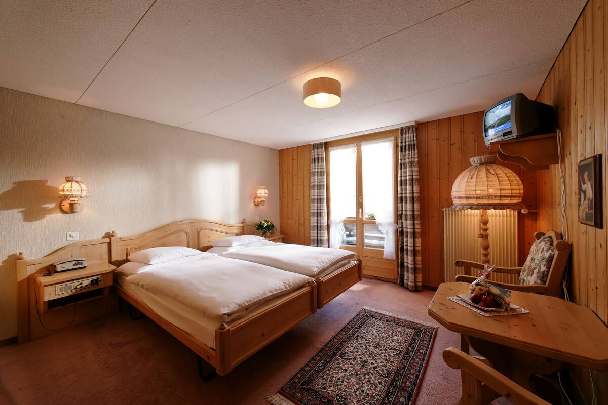 Une chambre avec deux lits, un bureau en bois, une chaise, une lampe et un téléviseur.