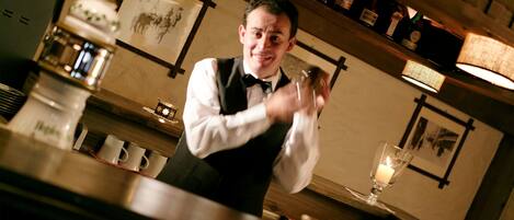 Un bar avec un barman, des étagères remplies de bouteilles et une bougie posée sur le comptoir.