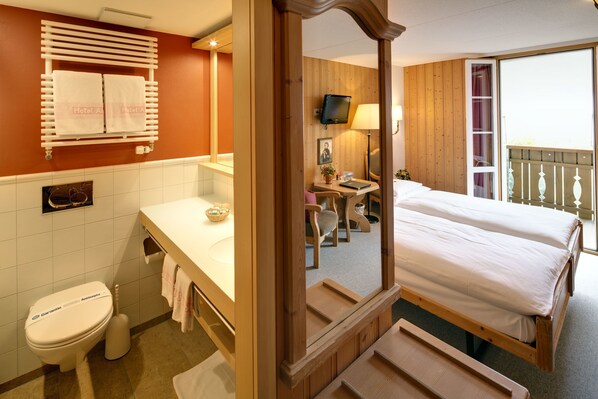 Ein Hotelzimmer mit einem hölzernen Bett, einem Badezimmer mit Toilette, Waschbecken und Spiegel.