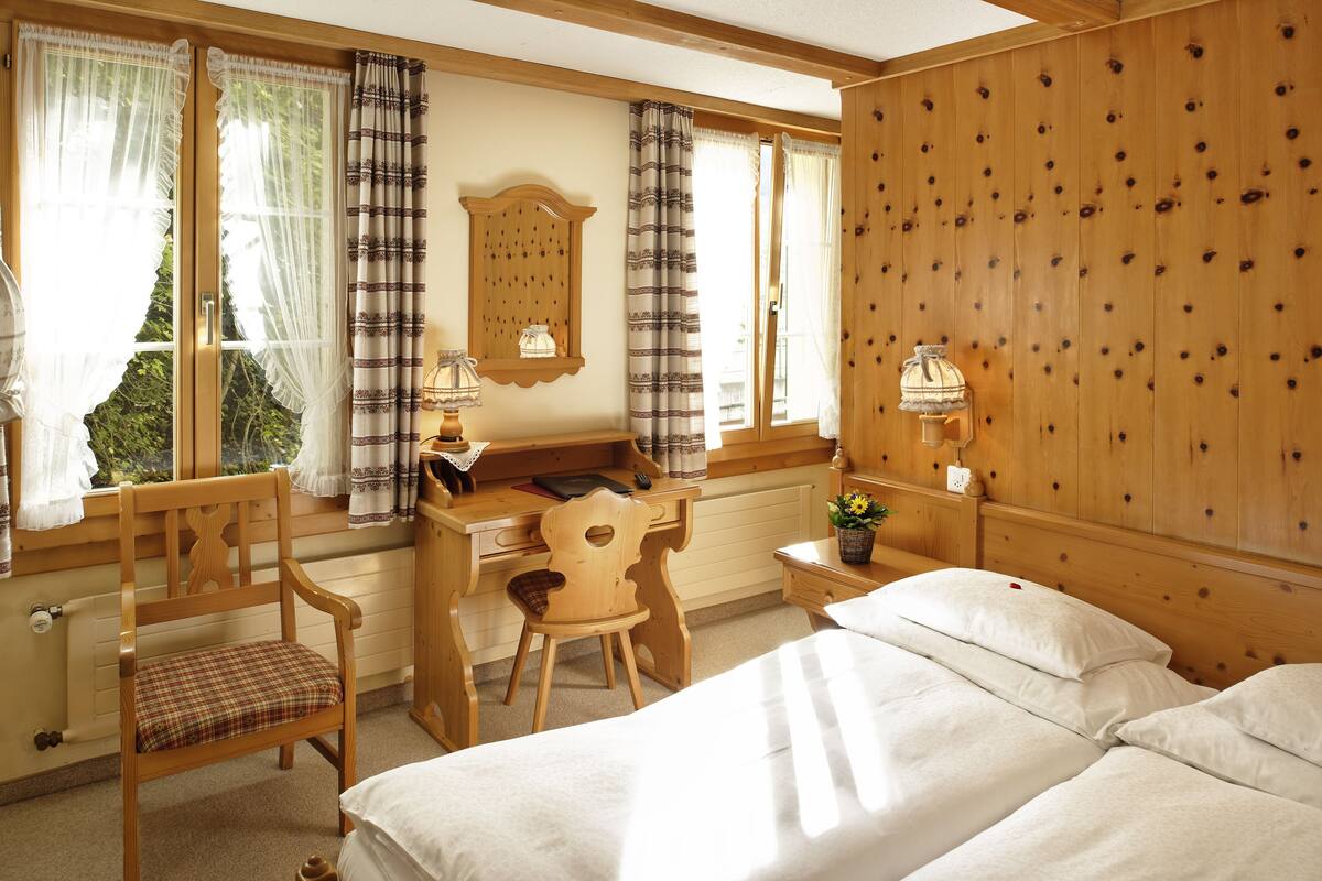 Une pièce confortable avec un bureau en bois, deux chaises, un lit et une fenêtre avec des rideaux.