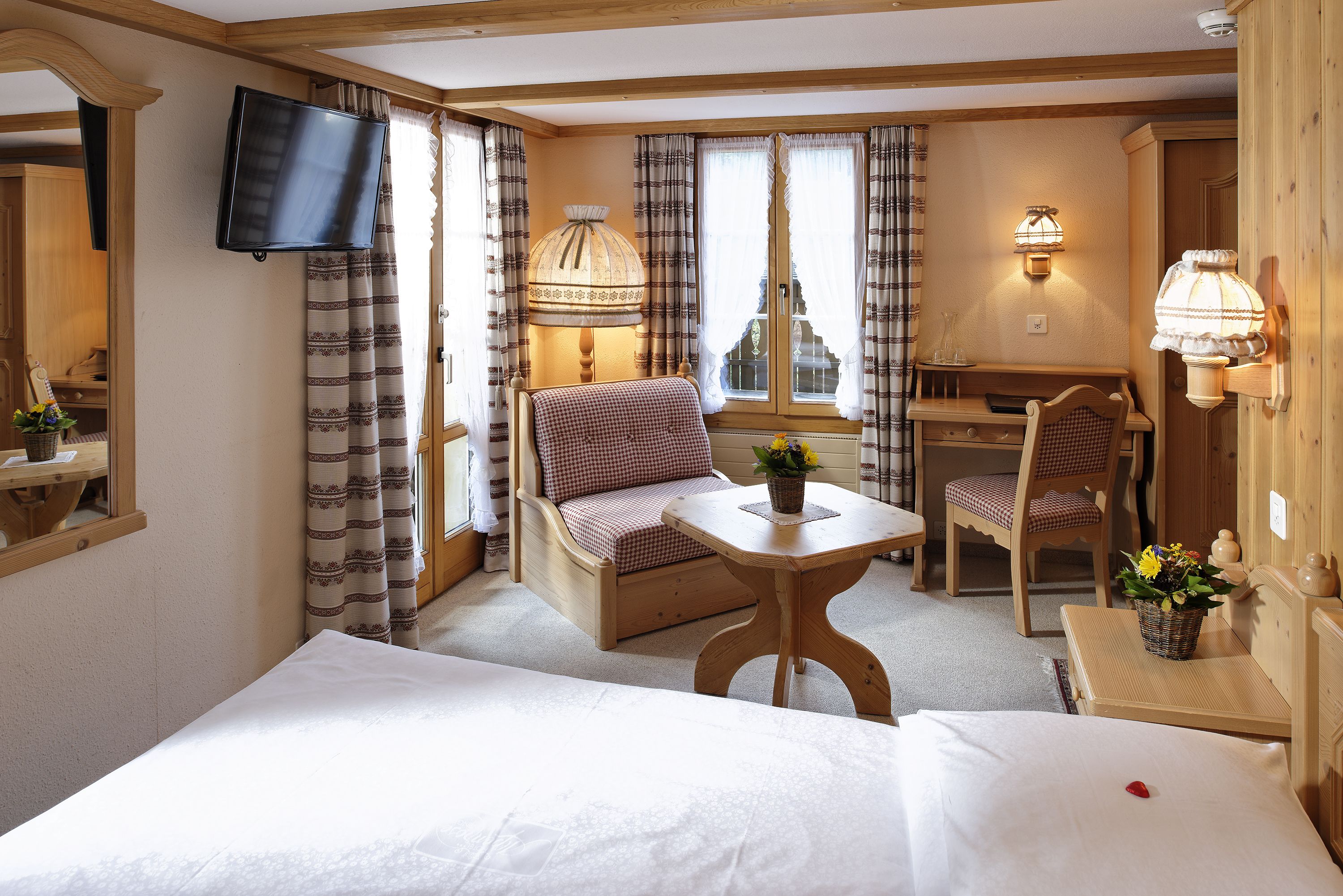 A hotel room with a bed, a desk, a chair, a TV, and a lamp.