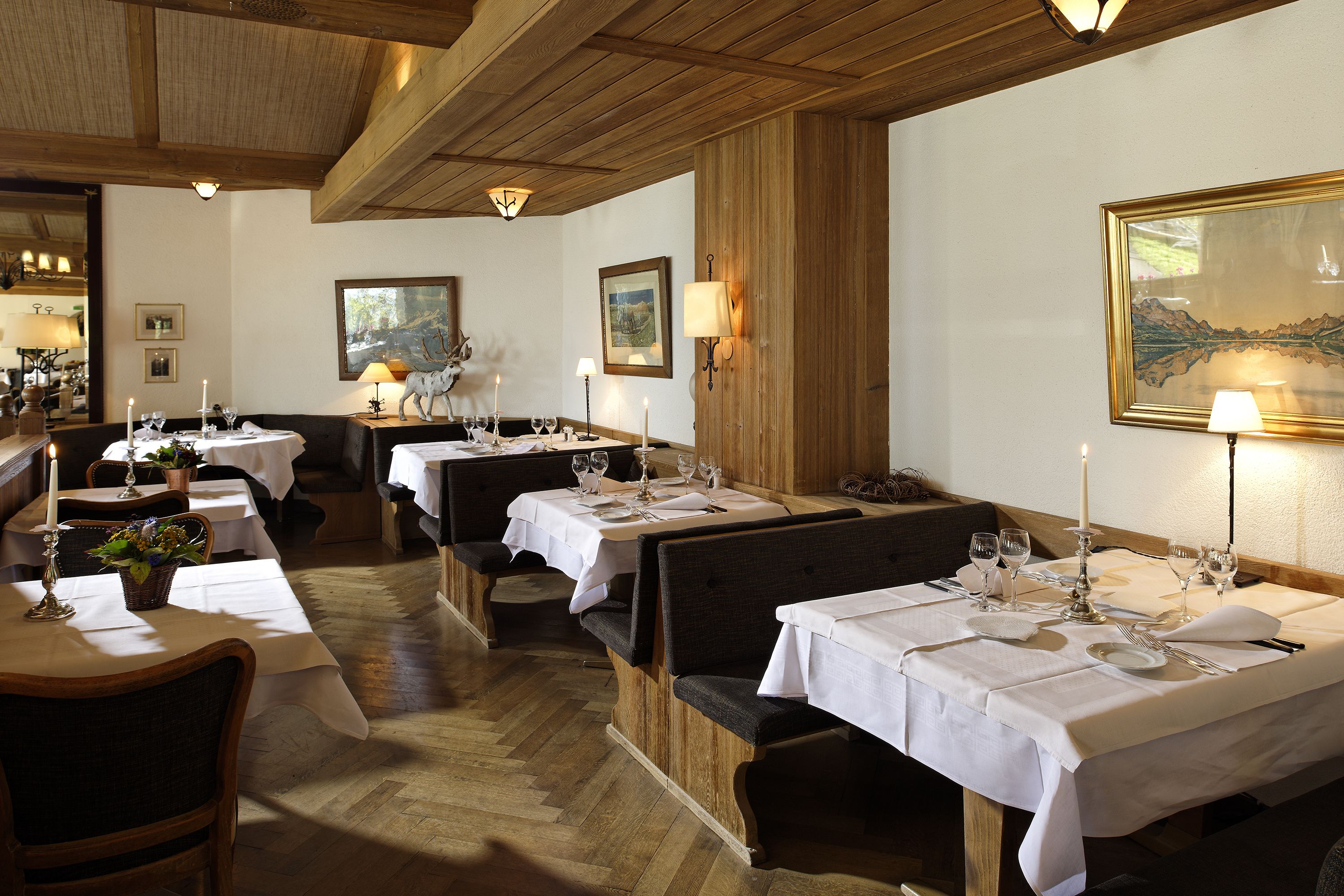 A restaurant with wooden tables and benches, white tablecloths, candles, and framed artwork on the walls.