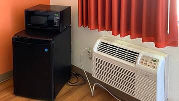 Una cuineta compacta amb microones i nevera de color negre, un aire condicionat blanc i una finestra amb cortines vermelles.