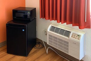 A compact refrigerator with a microwave on top, an air conditioner, and a power outlet on the wall.