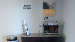 Una kitchenette con una cafetera, un cubo de basura y un cartel de café en la pared.