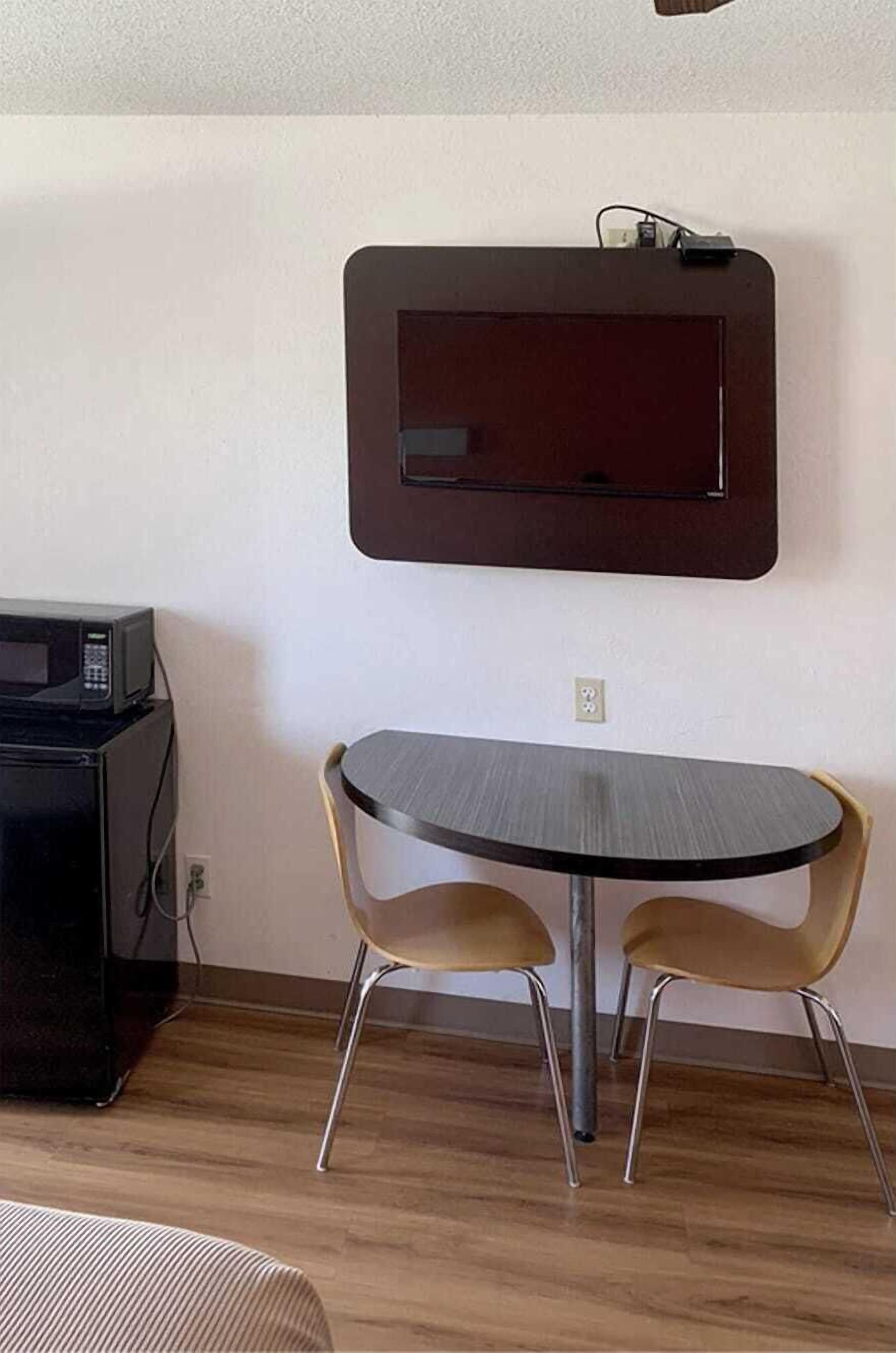 Una habitación pequeña con una mesa redonda y dos sillas, un microondas y un televisor instalado en la pared.