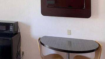 Una habitación pequeña con una mesa redonda y dos sillas, un microondas y un televisor instalado en la pared.
