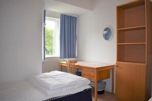 A bedroom with a bed, a desk, a chair, a wardrobe, and a window with curtains.