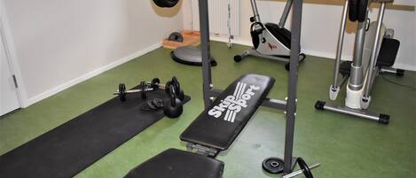 Un gimnasio con una prensa de banca, mancuernas y un soporte para barras.