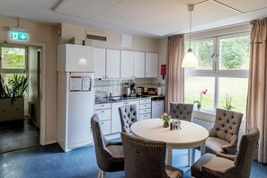 Una cocina moderna con armarios blancos, un comedor con una mesa redonda y cuatro sillas, y vistas a la vegetación a través de amplios ventanales.