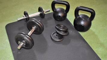 Un juego de mancuernas negras, kettlebells y discos de pesas sobre una colchoneta negra.