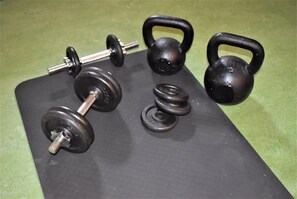 A set of black dumbbells, kettlebells, and weight plates on a black mat. - Wendelsberg STF Hotell (Mölnlycke)