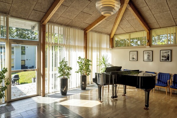 Una habitación amplia con un piano de cola, ventanas grandes y vistas al exterior.