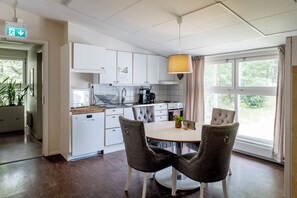 Een moderne keuken met witte kastjes, een eettafel met stoelen, een hanglamp en uitzicht op groen.