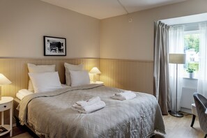 A hotel room with a large bed, two bedside tables with lamps, a framed picture on the wall, and a view of the outdoors through a window. - Wendelsberg STF Hotell (Mölnlycke)