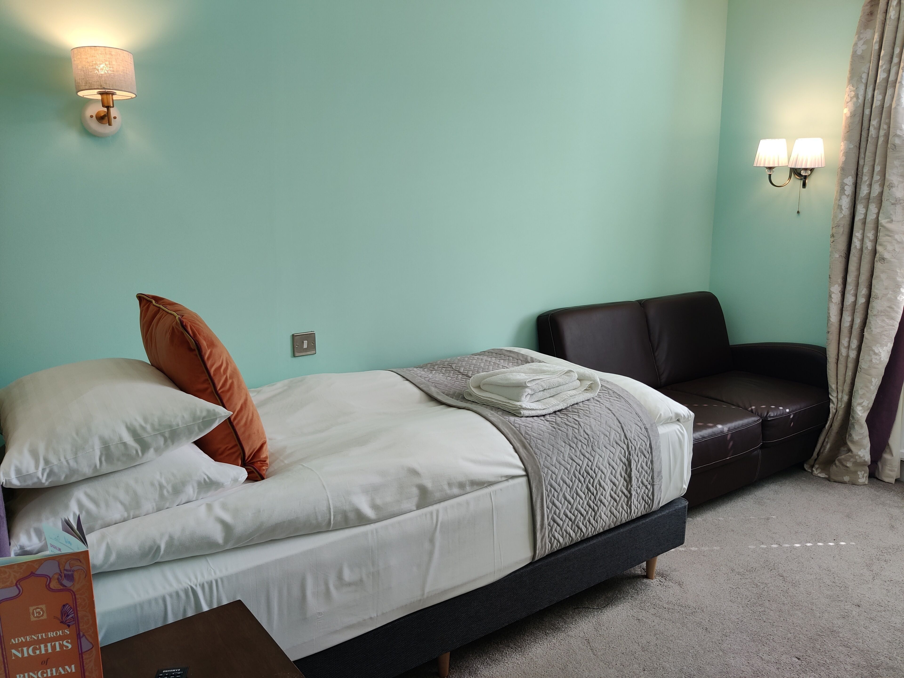 A bedroom with a bed, a sofa, and two wall-mounted lamps.