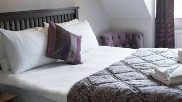 Una cama bien hecha con una colcha estampada y almohadones, un cabecero de madera y una ventana con cortinas.