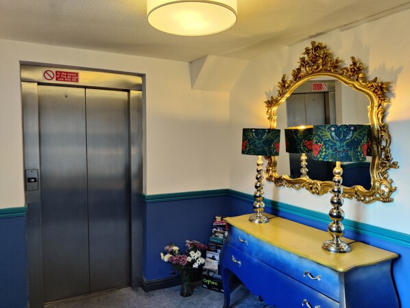 A room with a blue and gold dresser, a mirror with ornate gold frame, and a closed elevator. - The Bingham Townhouse (Nottingham)