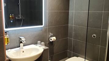 Casa de banho moderna com lavatório branco, sanita e cabine de duche com parede de vidro.