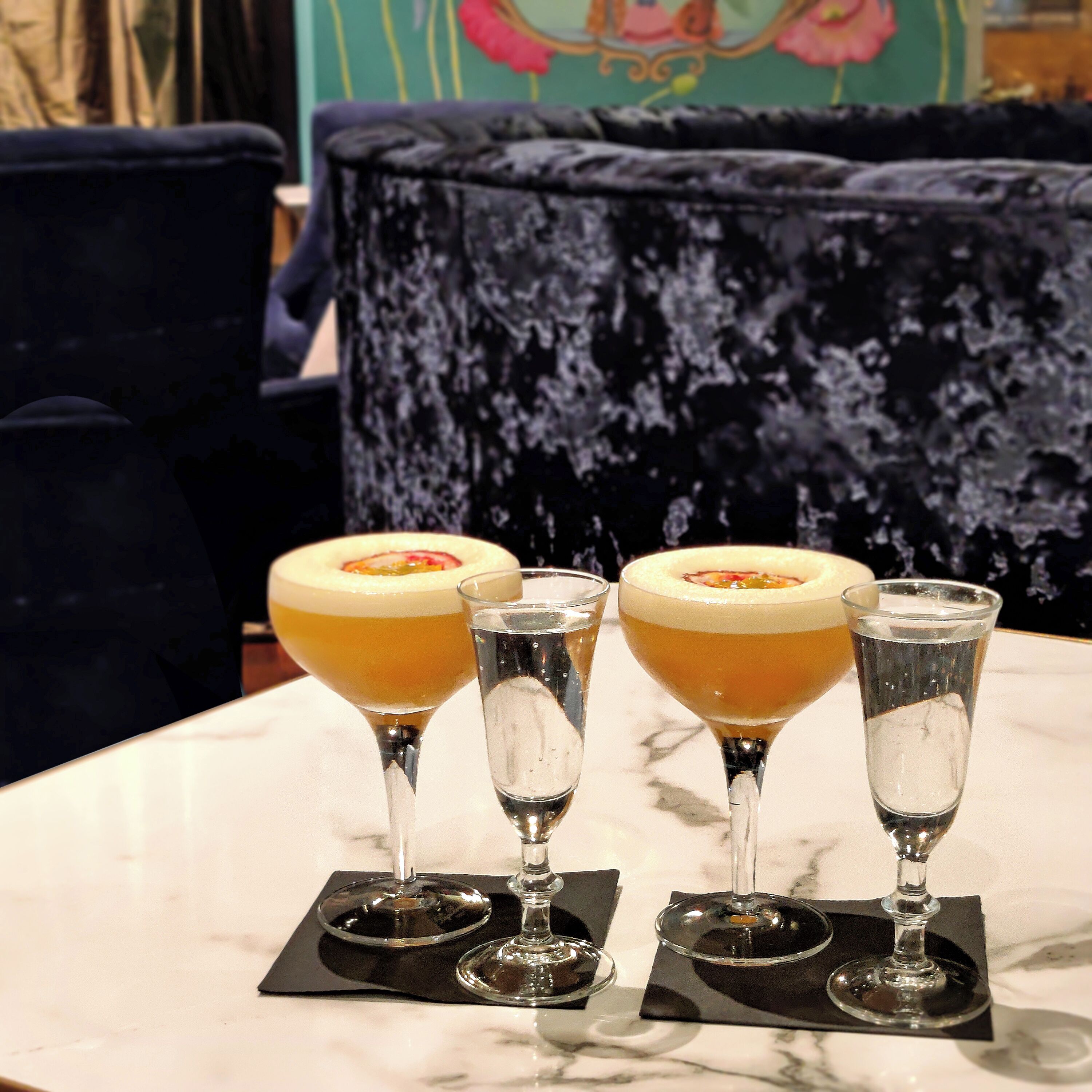 A table with three glasses of a yellow beverage, two of which have a garnish, and a clear glass with ice.