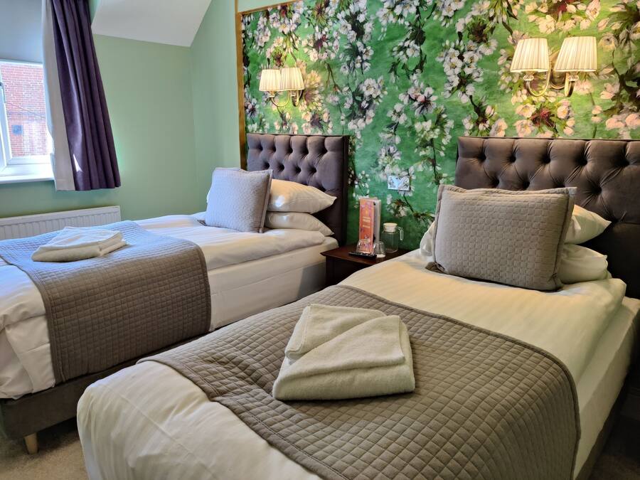 Habitación de hotel con dos camas, papel tapiz floral verde y cabecera oscura.