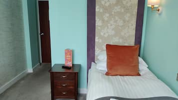 Un dormitorio con una cama, una mesita de noche, una lámpara y una puerta.