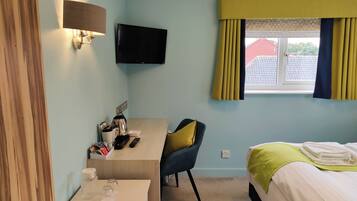Habitación de hotel con cama, escritorio con silla, televisor montado en la pared y ventana con cortinas.