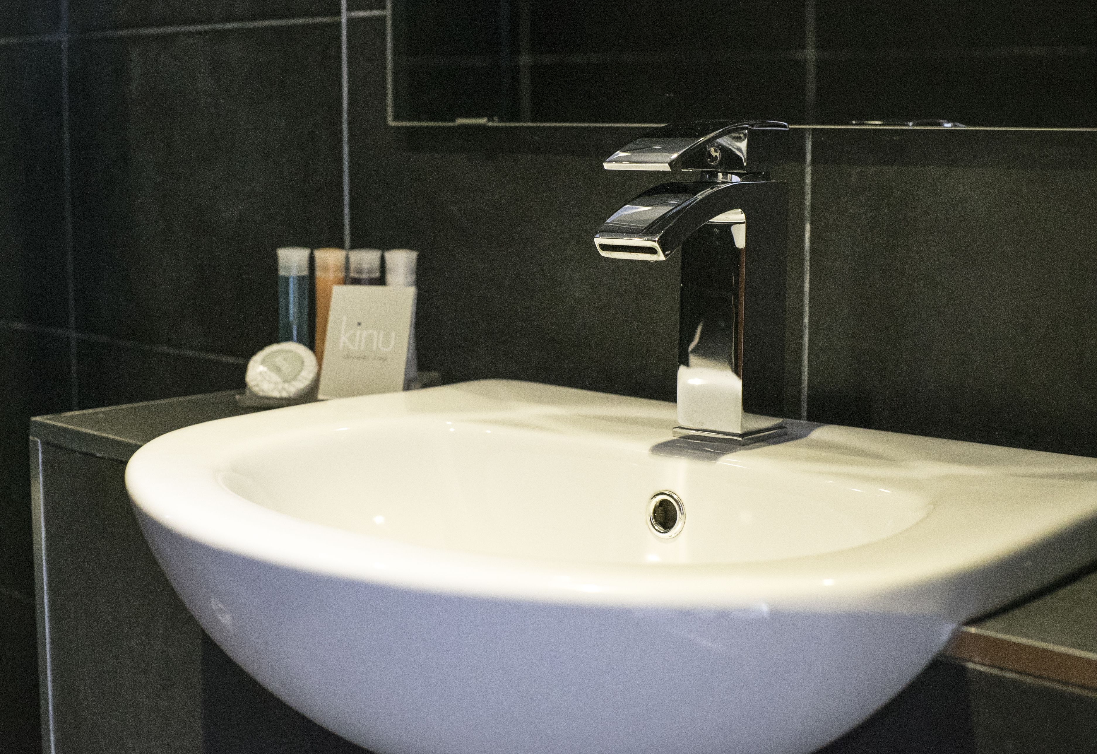 A modern bathroom with a white sink, chrome faucet, and dark tiled walls.
