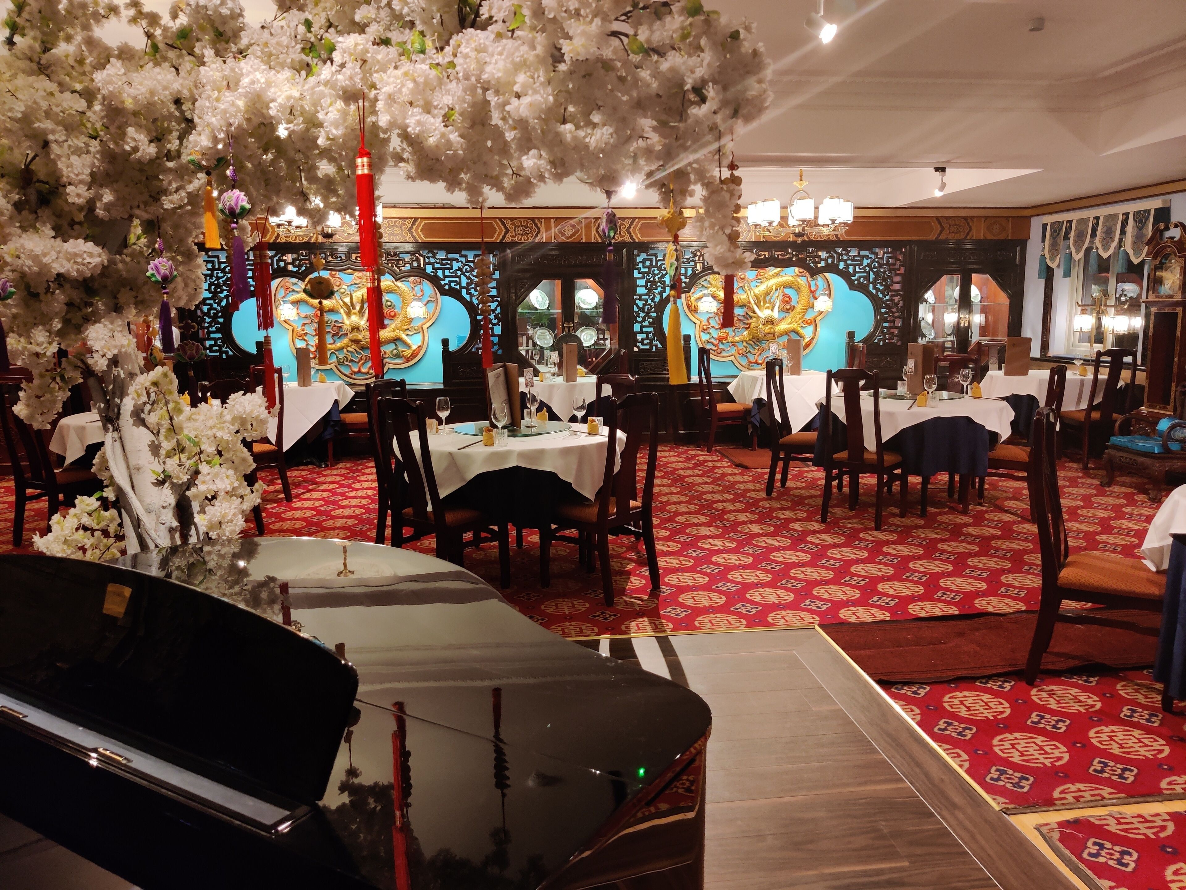 A restaurant with round tables, red patterned carpet, and traditional decor.
