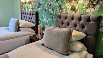 A hotel room with two beds, each with a tufted headboard, a nightstand with a remote control, and a wall with a floral wallpaper.