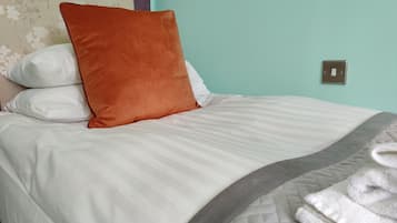 A neatly made bed with white and grey bedding, a brown accent pillow, and a folded white towel.