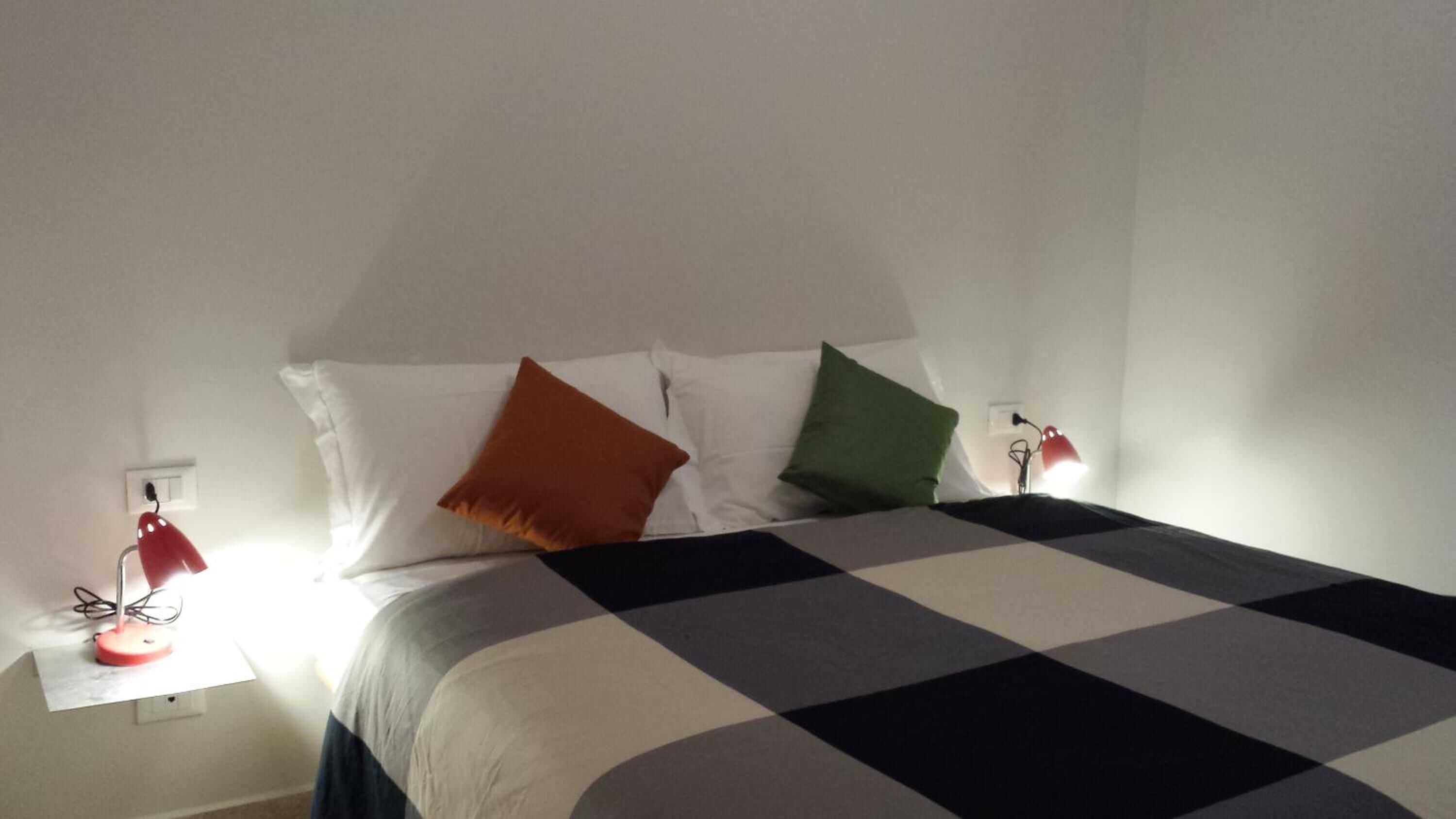 A neatly made bed with a checkered bedspread, two bedside lamps, and three pillows of different colors.