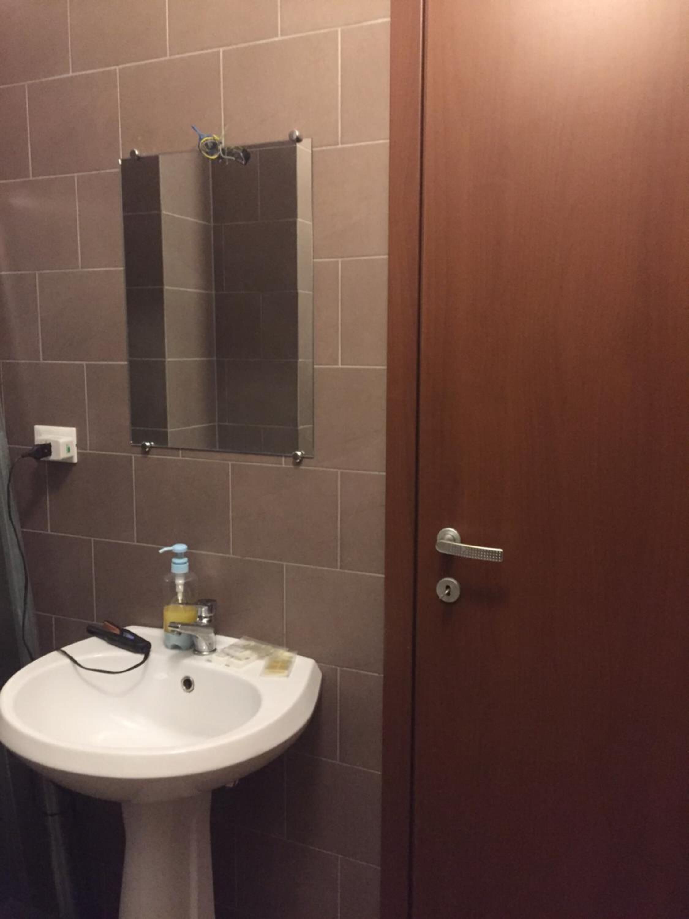 A bathroom with a white pedestal sink, a mirror above it, and a wooden door.