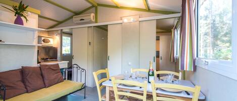 A compact room with a sofa, dining table, chairs, a small kitchenette, and a window with curtains.