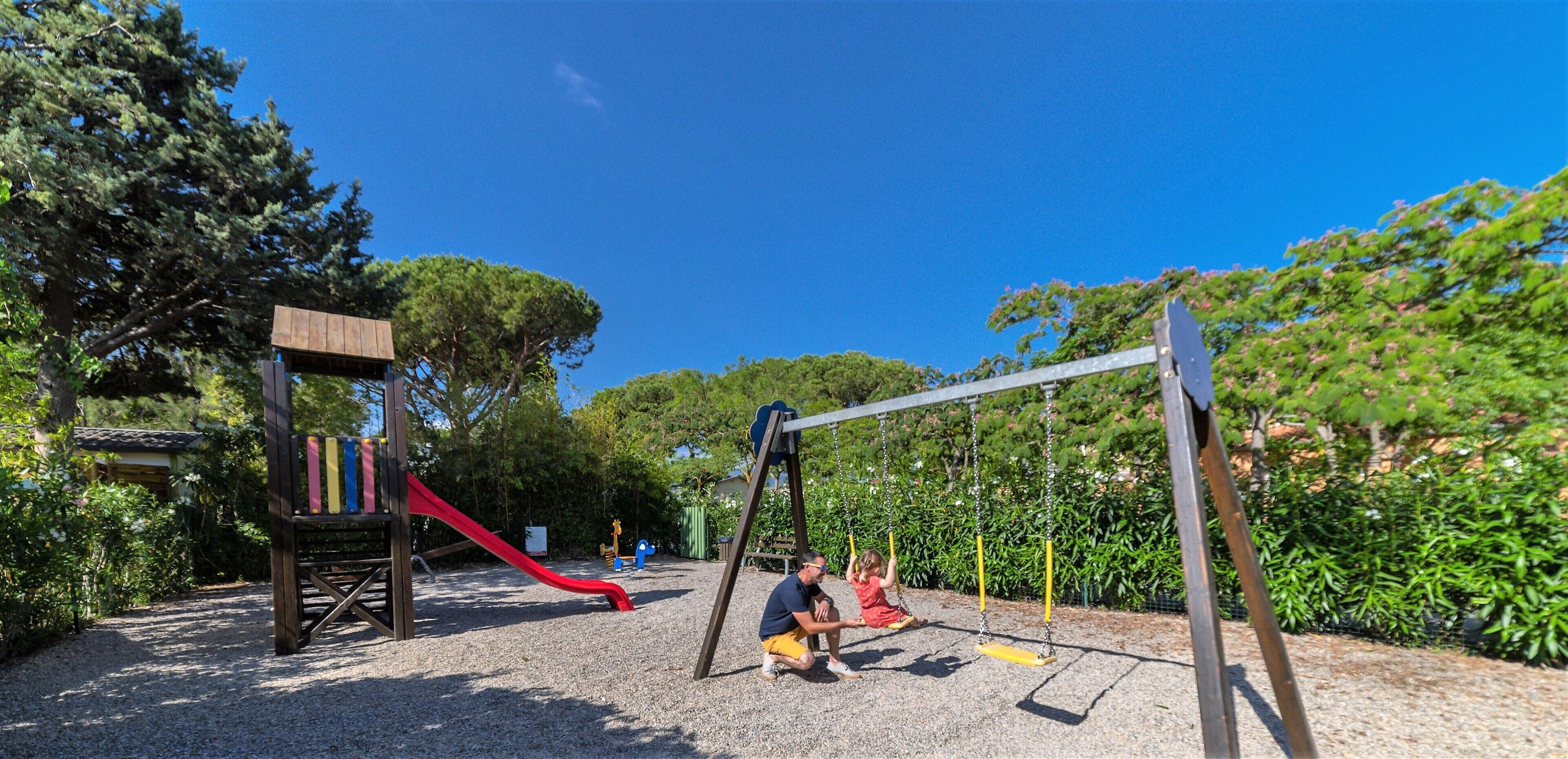 Une aire de jeux avec un toboggan, des balançoires et une structure de jeu en bois.