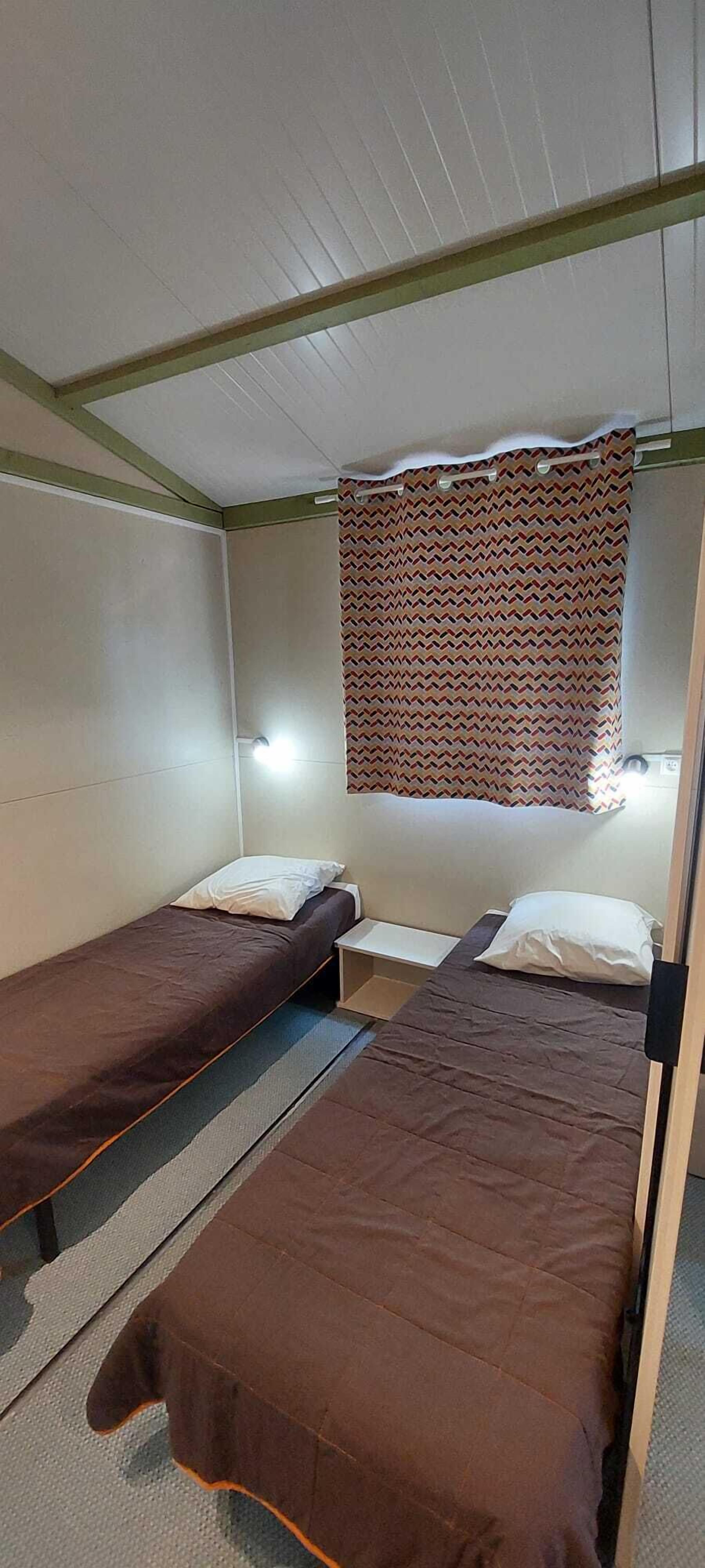 Ein Schlafraum mit zwei Einzelbetten, einem gemusterten Vorhang und einem kleinen Tisch.